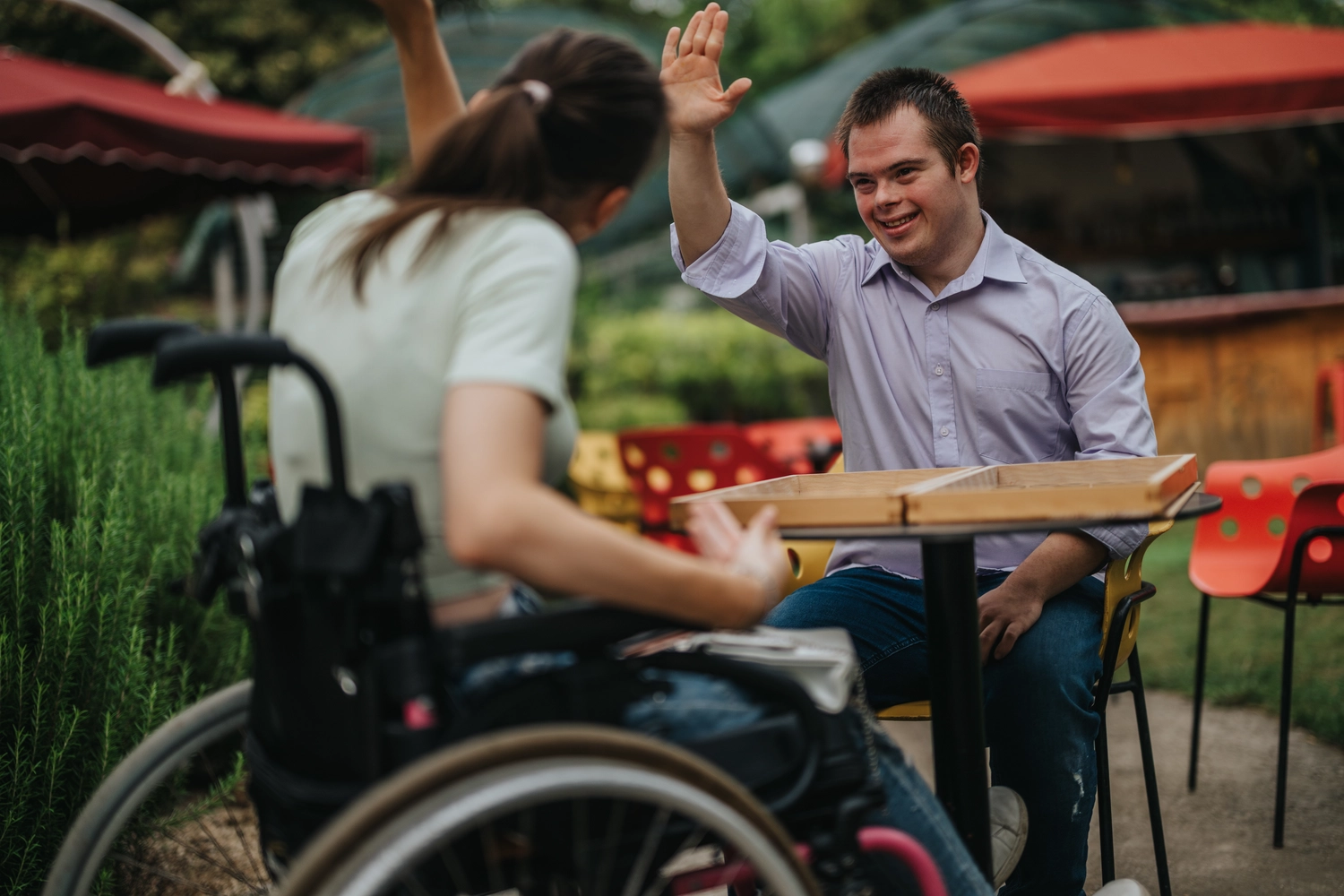 Odenwald - Stiftung Naturschutz - barrierefrei - Ein Junge mit Down-Syndrom gibt einem Mädchen im Rollstuhl High-Fives, während er an einem Tisch im Freien Backgammon spielt.